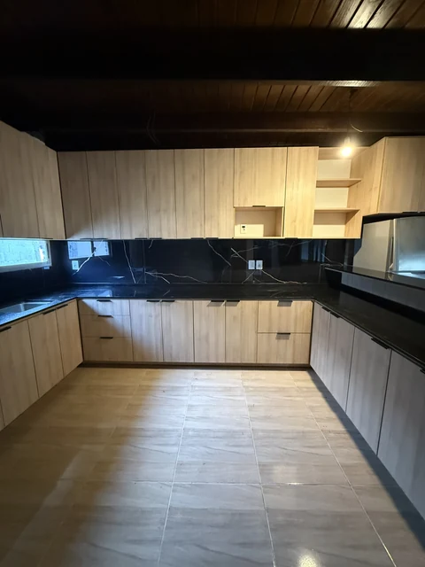 Vista interior de la cocina con muebles en tono madera, cajones y mesada negra.