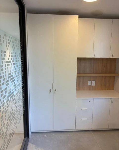 Mueble blanco a medida con armario alto, cajones, puertas con cerradura y nicho de aspecto madera.